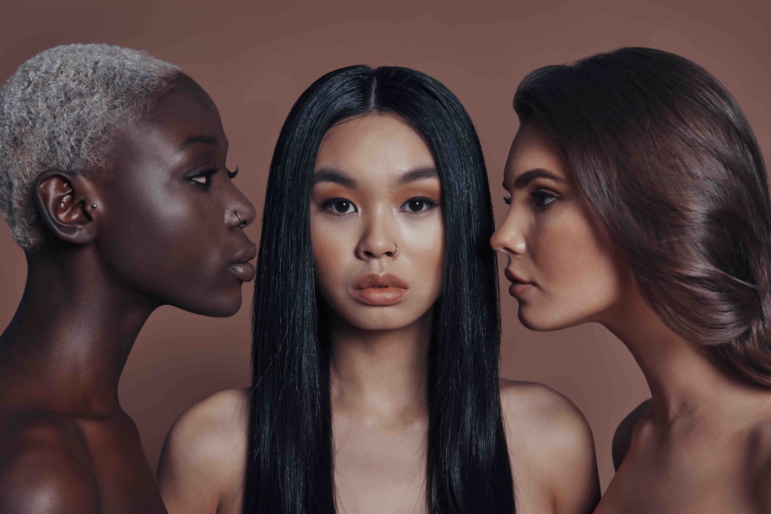 Gorgeous beauties. Three attractive young women looking at camera while standing against brown background